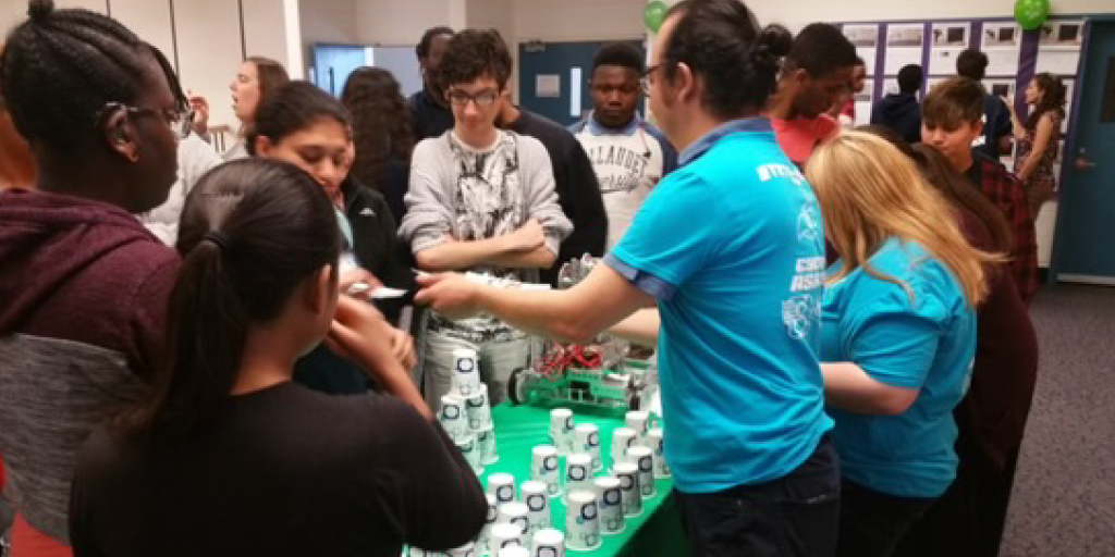 Gabriel shows off robots in front of a group of students.