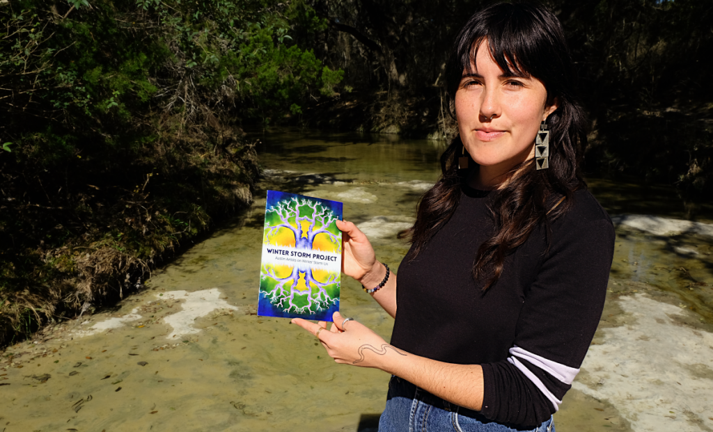 A photo of Gaby holding up The Winter Storm Project anthology in front of a creek.