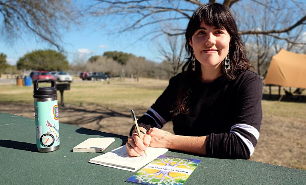 A photo of Gaby smiling at a table in Mary Moore Searight Metropolitan Park. She is holding a pen to her notebook.