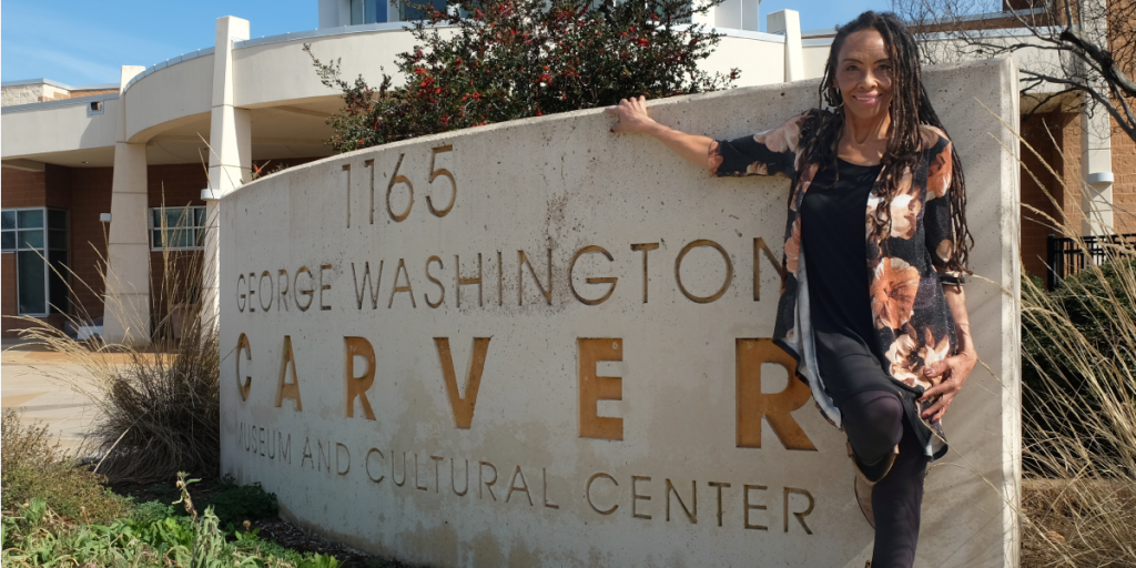 Harvé poses in front of the sign for the George Washington Carver Museum and Cultural Center.
