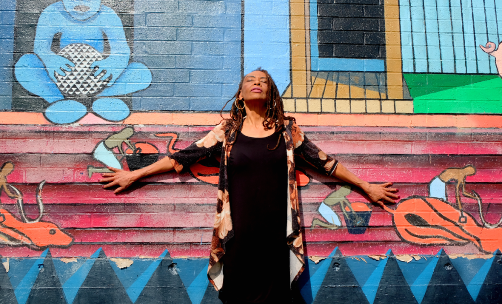 Harvé stands looking up against a colorful mural at the Carver Branch of Austin Public Library.