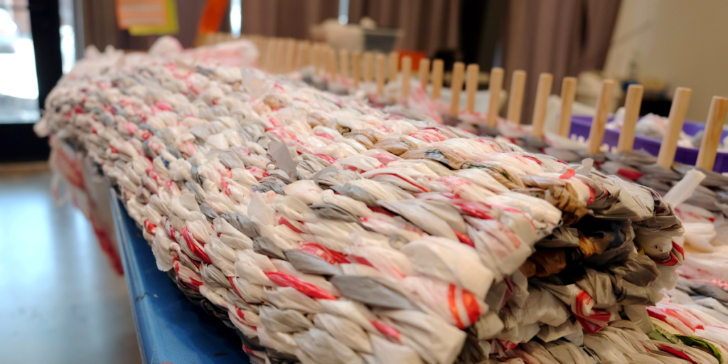 A rolled up sleeping mat attached to a wooden peg loom.