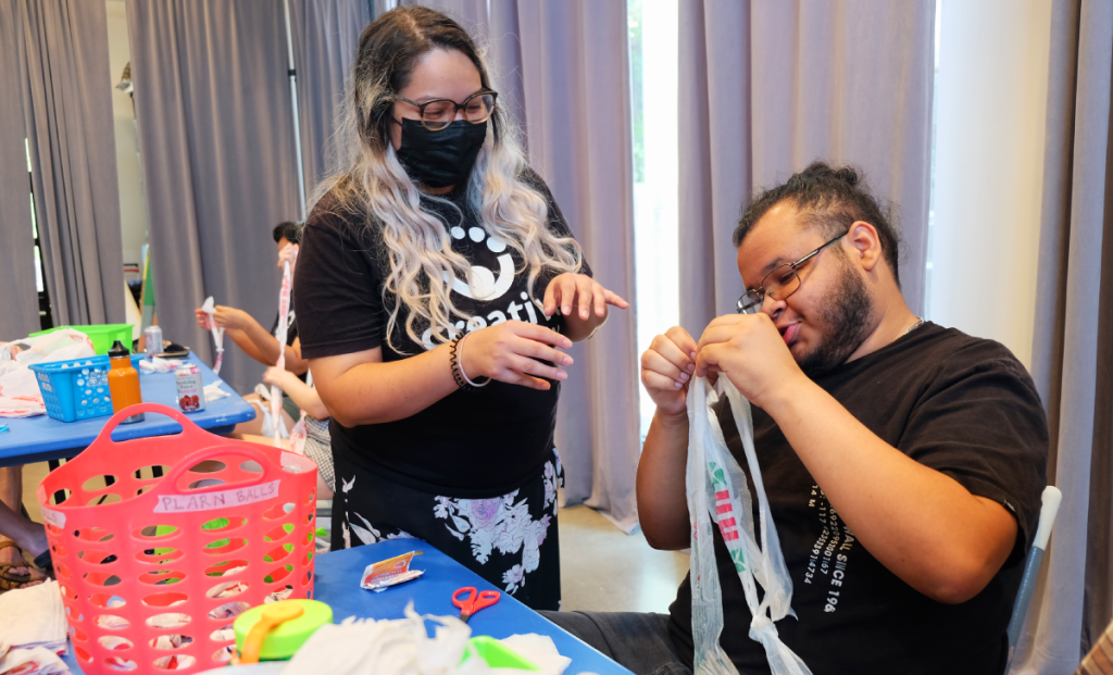 Kiana smiles as she reviews a selection of plarn made by a weaving circle attendee seated next to her.