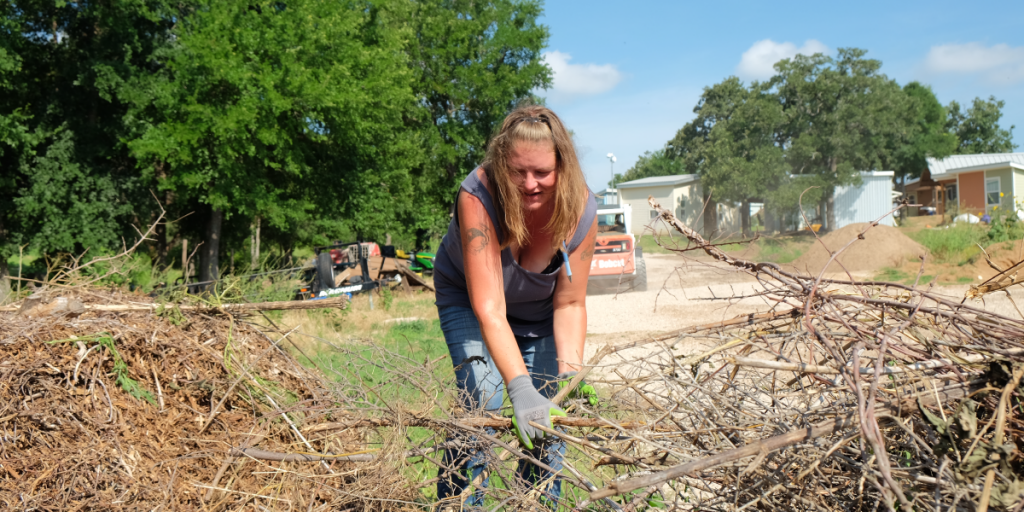 Leatha leans down to moves brush from a pile.