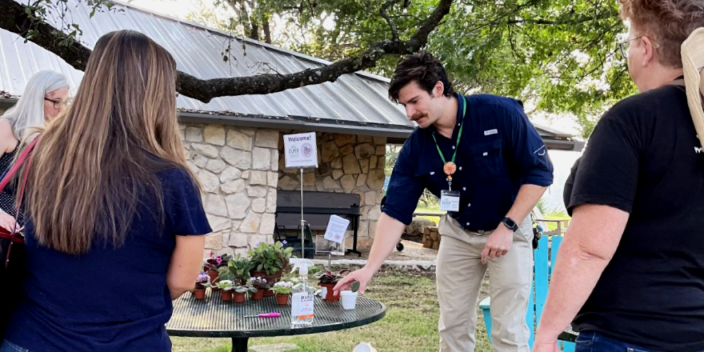 Matthew points out plants on a table with people gathered around him.