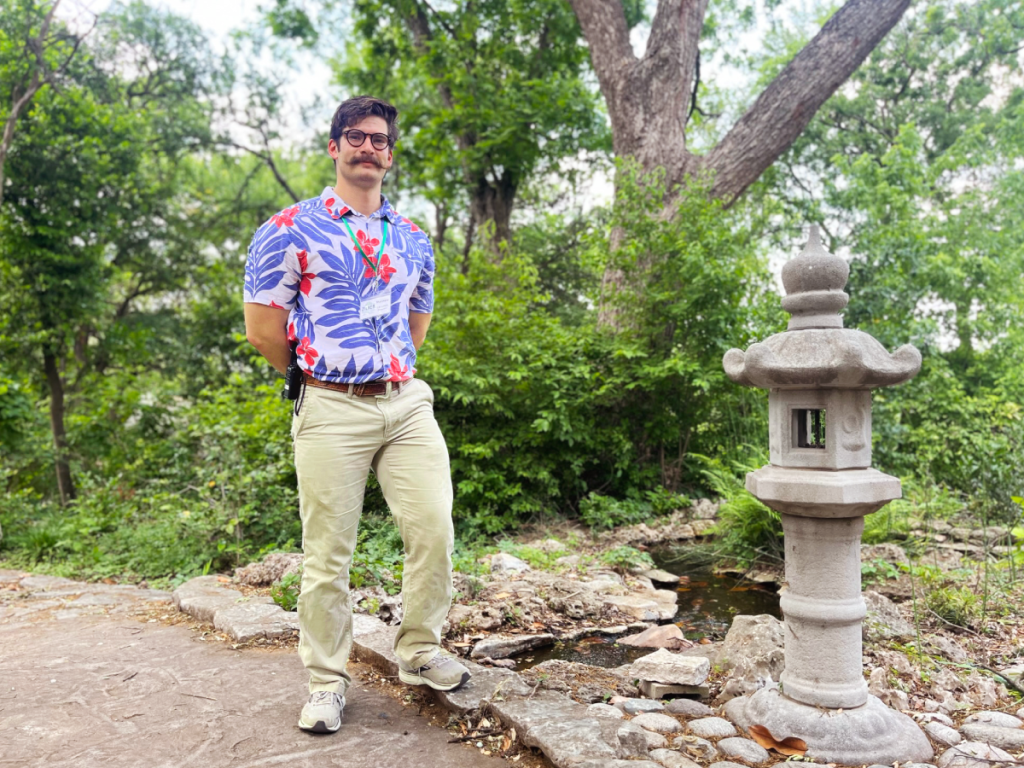 Matthew stands with lots of green foliage behind him.