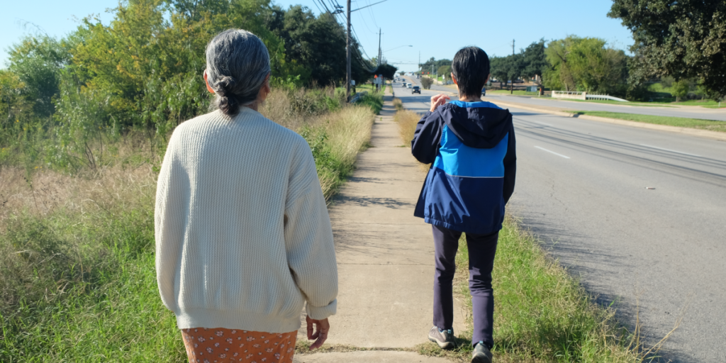 Niki and Himadri walk away from the camera down Cameron Road towards the bus stop.