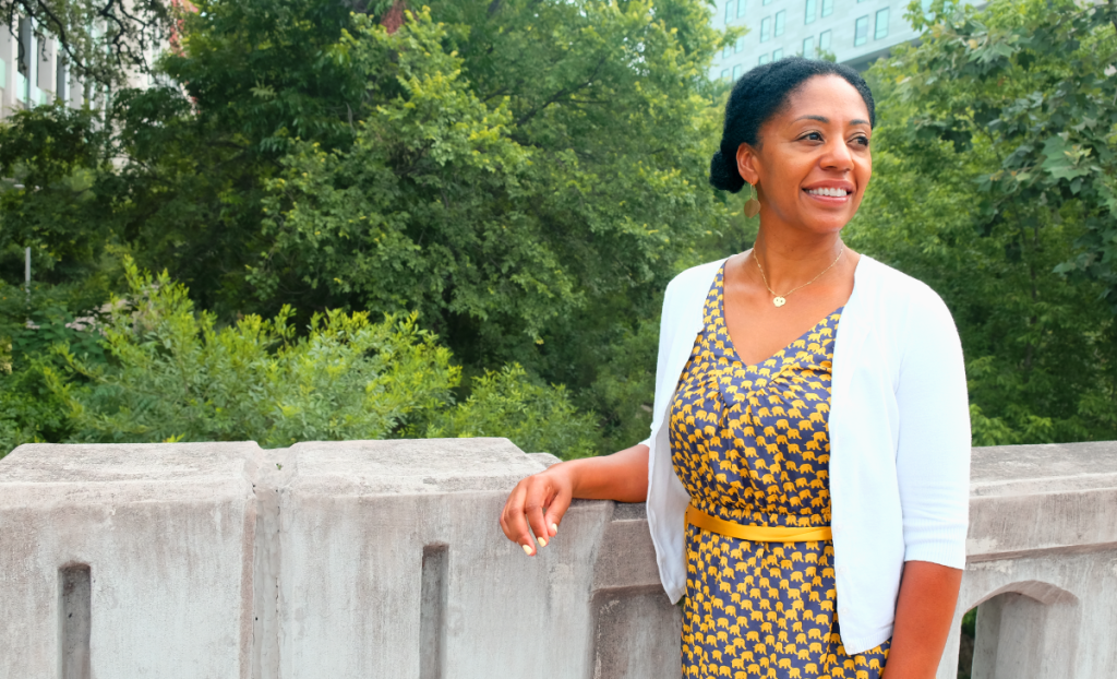 Nitakuwa stands on a bridge over Waller Creek looking in the distance and smiling.