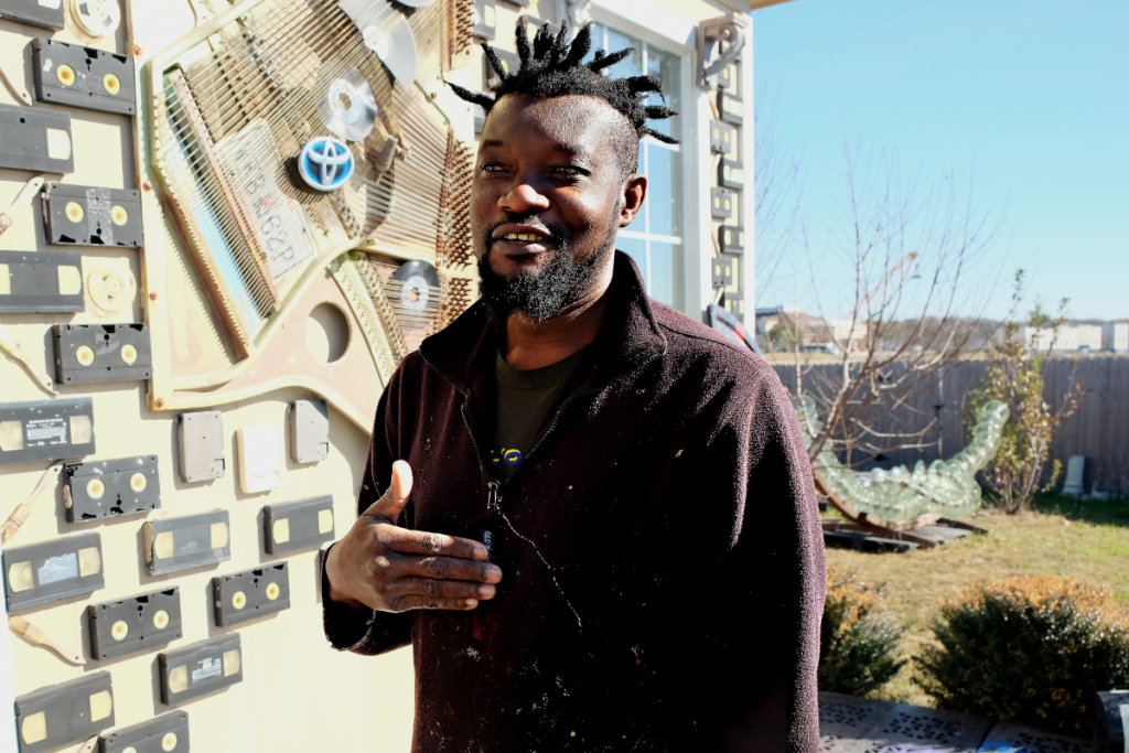 A photo of Olaniyi speaking with us in front of his studio. The studio is decorated with VHS tapes.