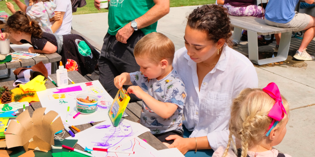 A woman holds a young boy on her lap. The boy is coloring with markers.