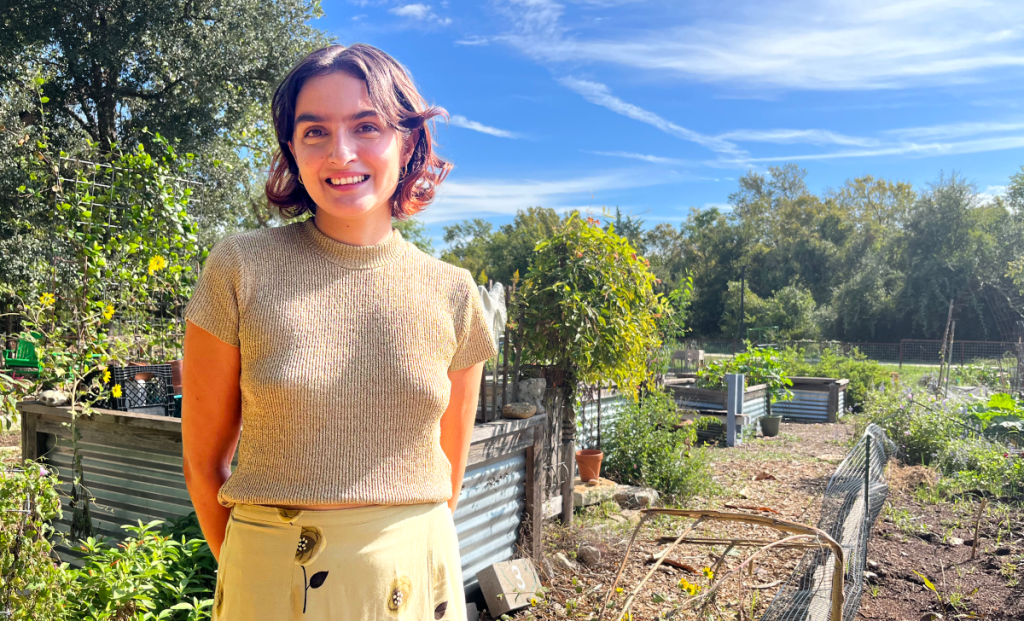 Reza stands outside at a community garden smiling.