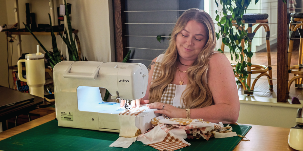 Shelby sits in her home studio, sewing pieces of fabric together for a current clothing project.