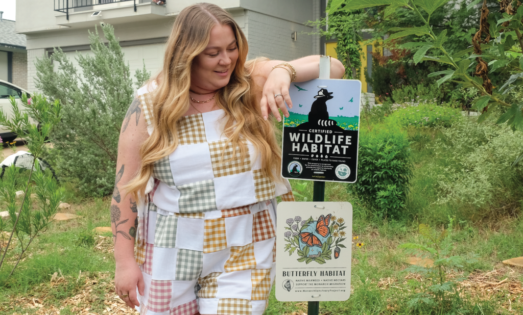 Shelby poses next to signs in her yard that read, “Certified Wildlife Habitat” and “Butterfly Habitat.”