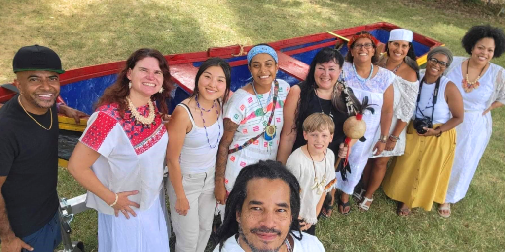 A group of people pose for a selfie in front of a small colorfully painted boat.