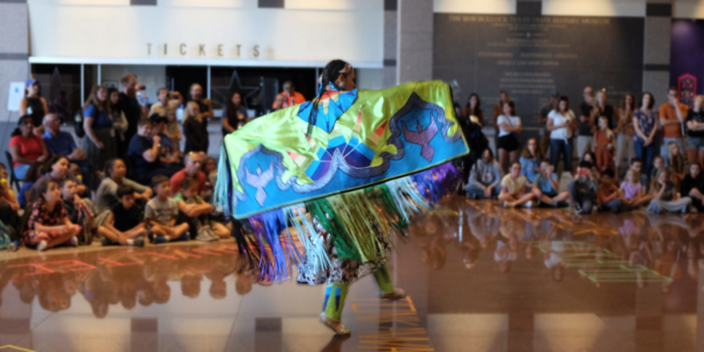 A woman dances with a very colorful shawl in the center of a group of students.