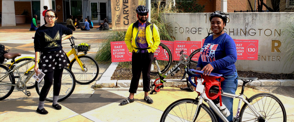 A photo of Stephanie with her bicycle outside of the George Washington Carver Museum. Other people on bicycles stand around her.