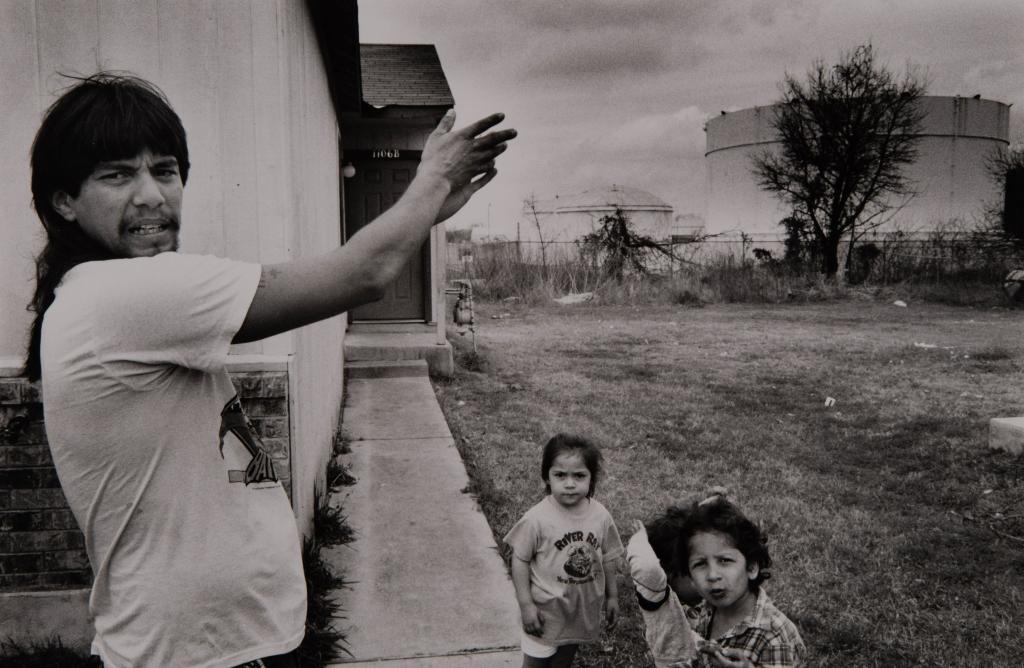 An East Austin resident shows the proximity of a tank behind their house. A few young children stand near him.