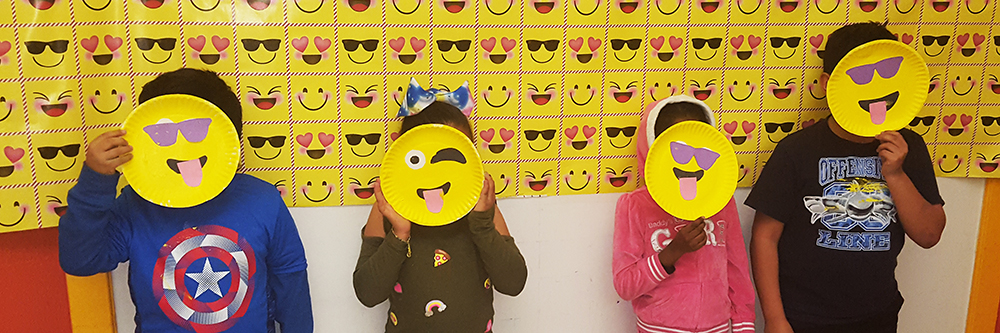 Kids posing with emoji faces they made from paper plates.