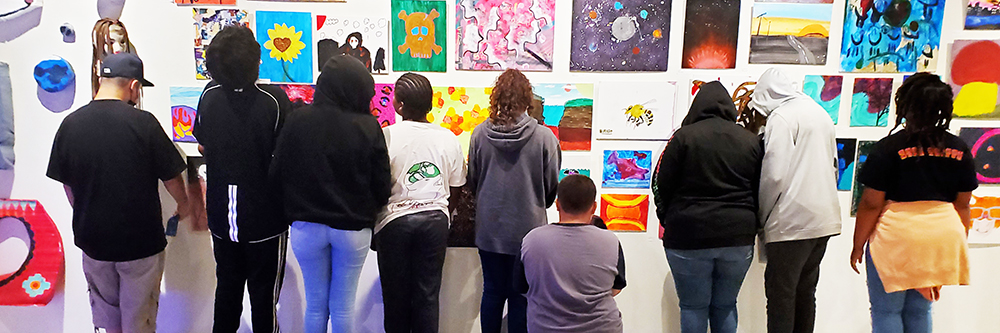 Teens observing their artwork hung up on a wall. 