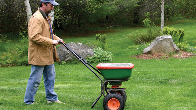 A man fertilizing a lawn with a broadcast spreader