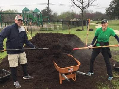 Photo: A man and woman smile at the camera while holding shovels full of mulch
