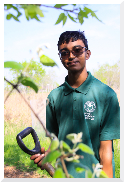 Anish holding a shovel in dappled shade outdoors