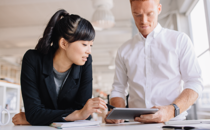 a man and woman looking over an ipad