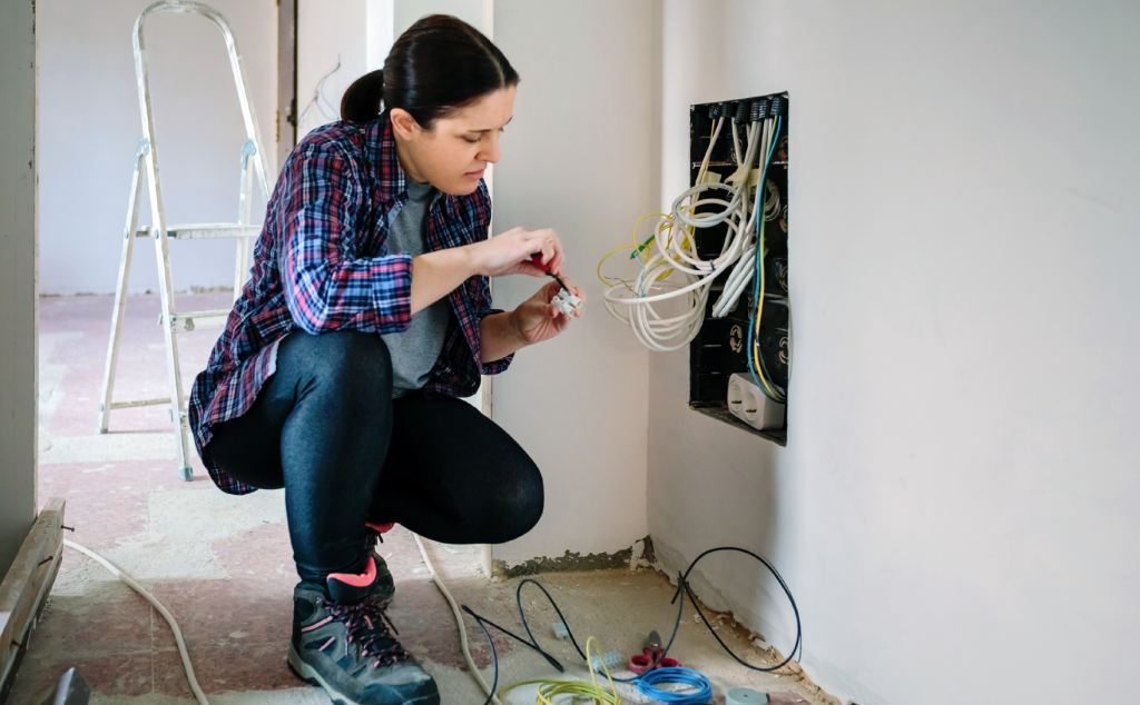woman working on wiring hanging out of a hole cut in the wall