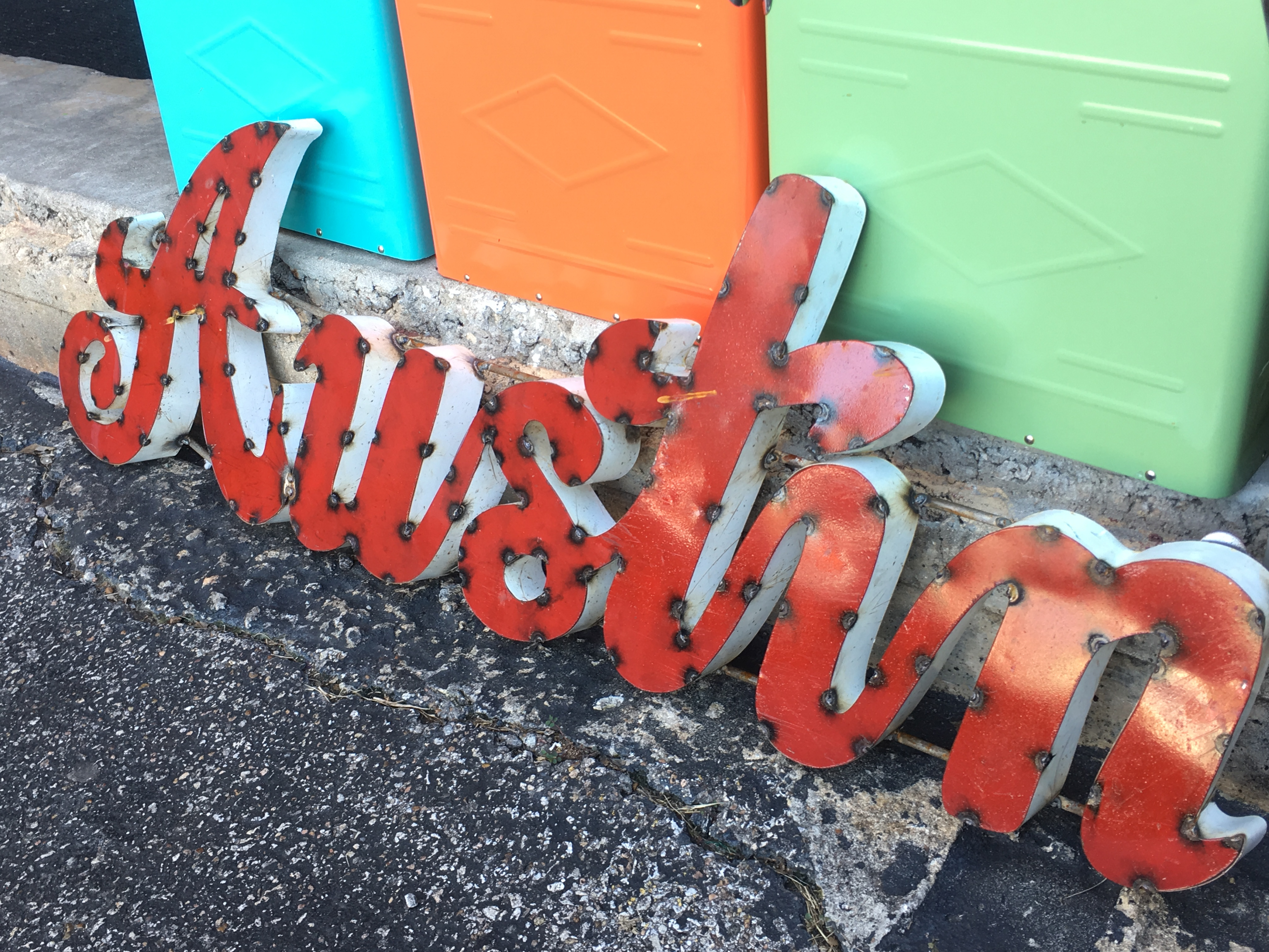 Red metal “Austin” sign with bright colors in background Red metal “Austin” sign with bright colors in background