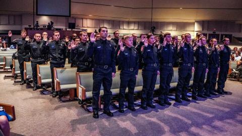 Uniformed officers standing in rows taking an oath.