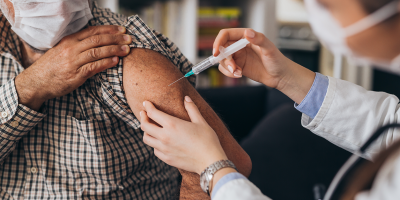 Man with long sleeve shirt rolled up to his shoulder being vaccinated by woman healthcare professional, both wearing masks