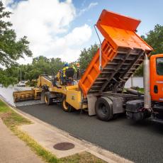 A bright orange truck applying a street resurfacing treatment to a neighborhood street