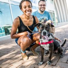 Two people pose with a dog in front of Austin Animal Center