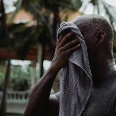 Image of man wiping his face with a towel outside on a hot, sunny day