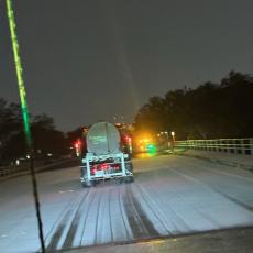 photo of ice on the street with a truck spreading de-icing brine in the foreground.