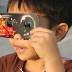 child holds solar eclipse glasses up to their eyes