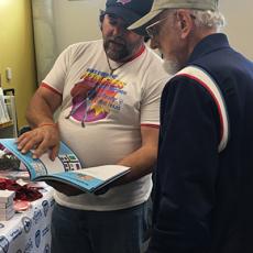 younger man wearing a hat shows an elderly man a manual on emergency preparedness.