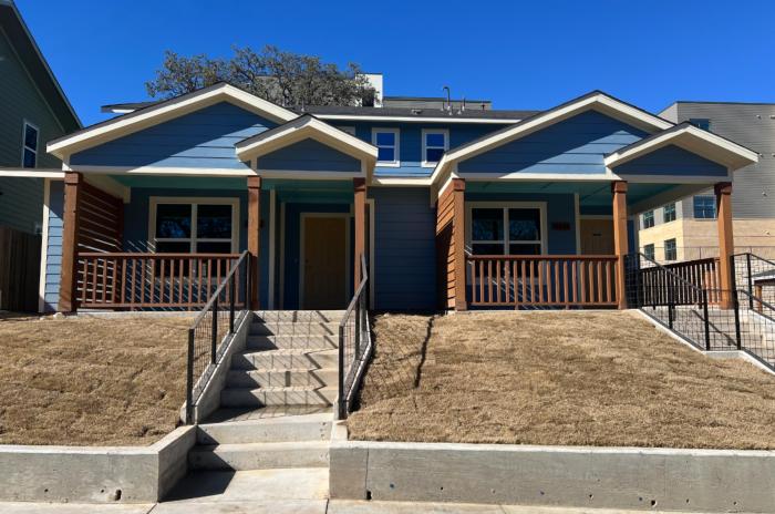 Image a two-story duplex with two townhomes. The exterior is blue with brown wood railings and columns on the covered front porch.