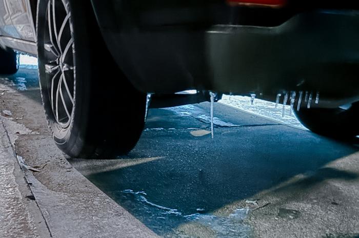 View of frozen bumper and tires of an SUV with icicles and frozen ground around it