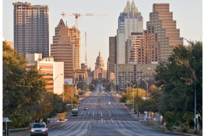 a street view photo of Downtown Austin with the Capital directly in the center of the photo with tall, sun kissed buildings to the left and right