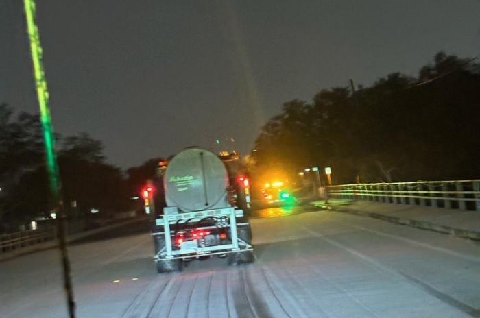 photo of ice on the street with a truck spreading de-icing brine in the foreground.