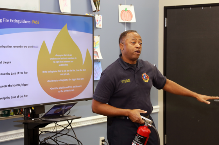 A photo showing an Austin firefighter demonstrating how to use a fire extinguisher at a classroom training for the community.