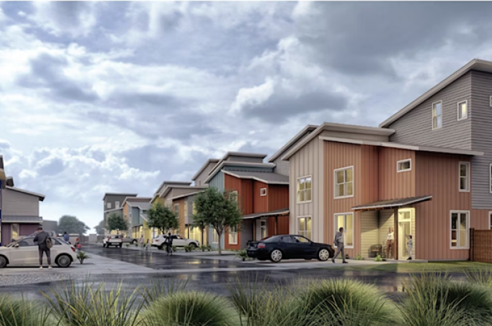 Rendering of Johnny Limon Village, a modern affordable housing community featuring colorful, two-story townhomes in shades of red, orange, yellow, and gray. The scene shows a clean, tree-lined street with parked cars, residents walking, and a partly cloudy sky overhead, evoking a welcoming and vibrant neighborhood atmosphere.