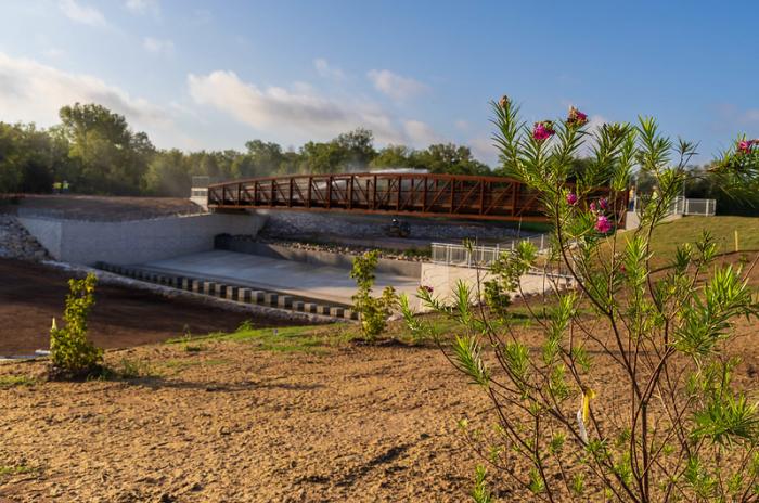New bridge over creek channel with newly-planted willow tree nearby.