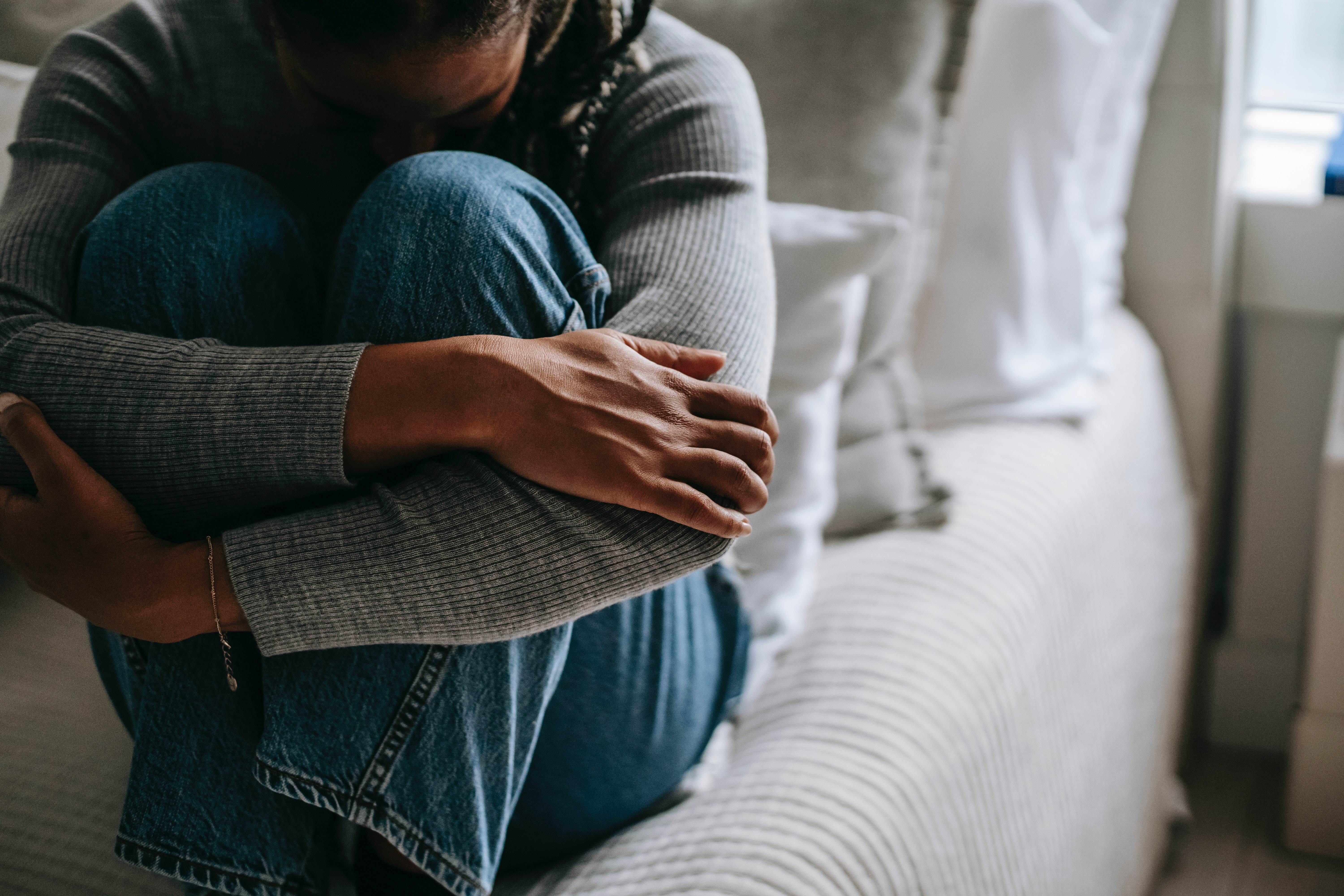 Woman sitting on bed holding her knees with her head bowed