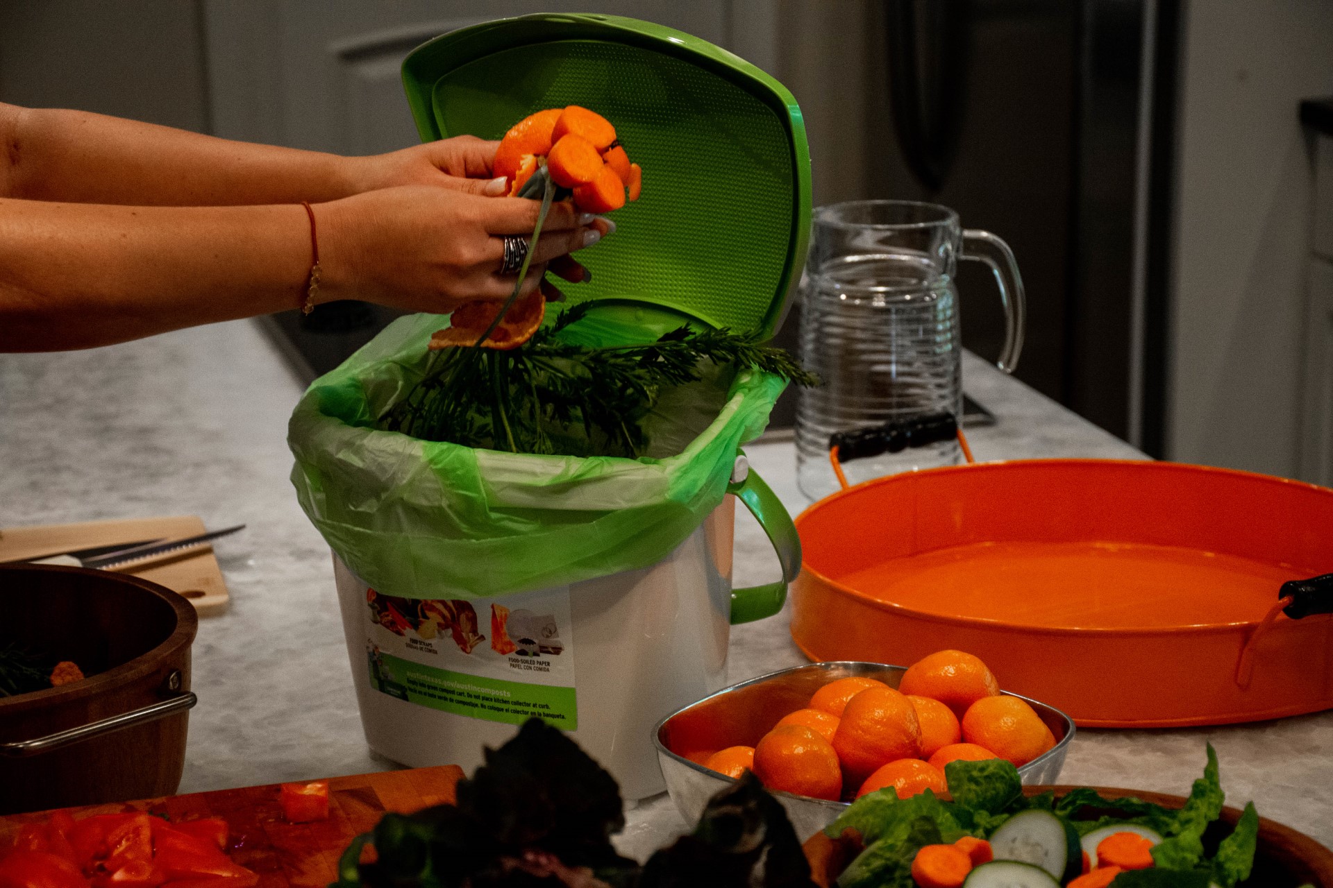 Two hands holding carrots above a composting bin.